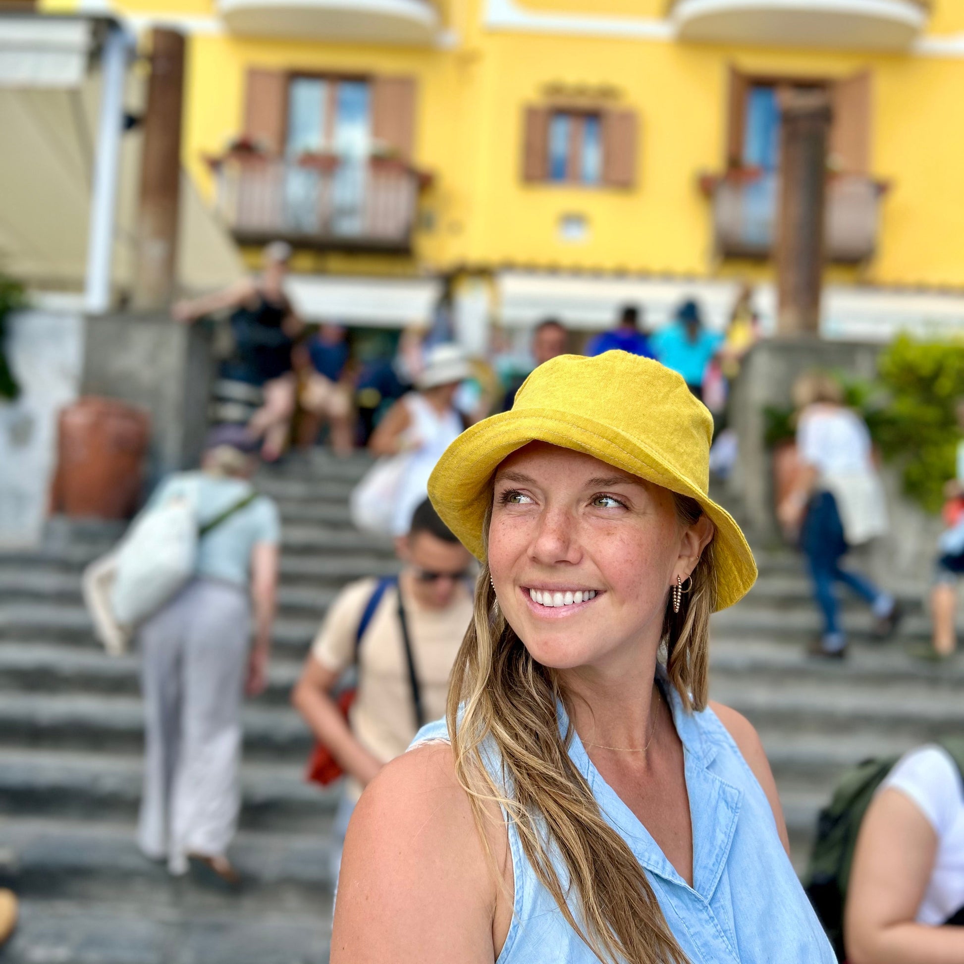 Woman wearing a yellow hat in an outdoor setting with a yellow building in the background