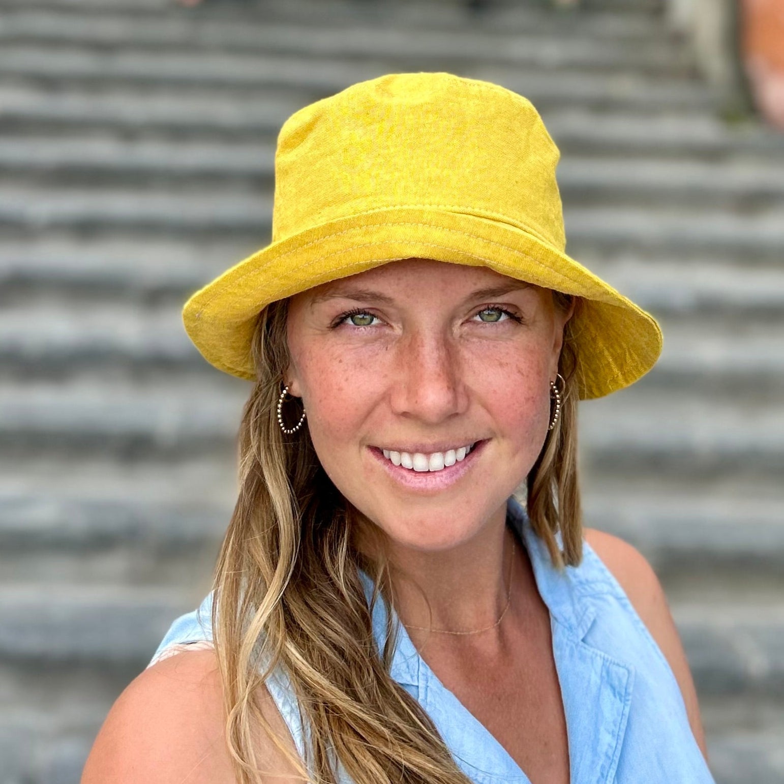 Woman wearing a yellow hat and blue top standing on steps with a yellow building in the background