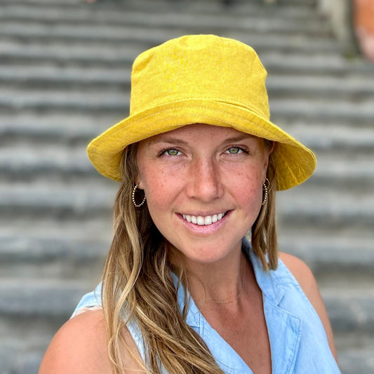 Woman wearing a yellow hat and blue top standing on steps with a yellow building in the background