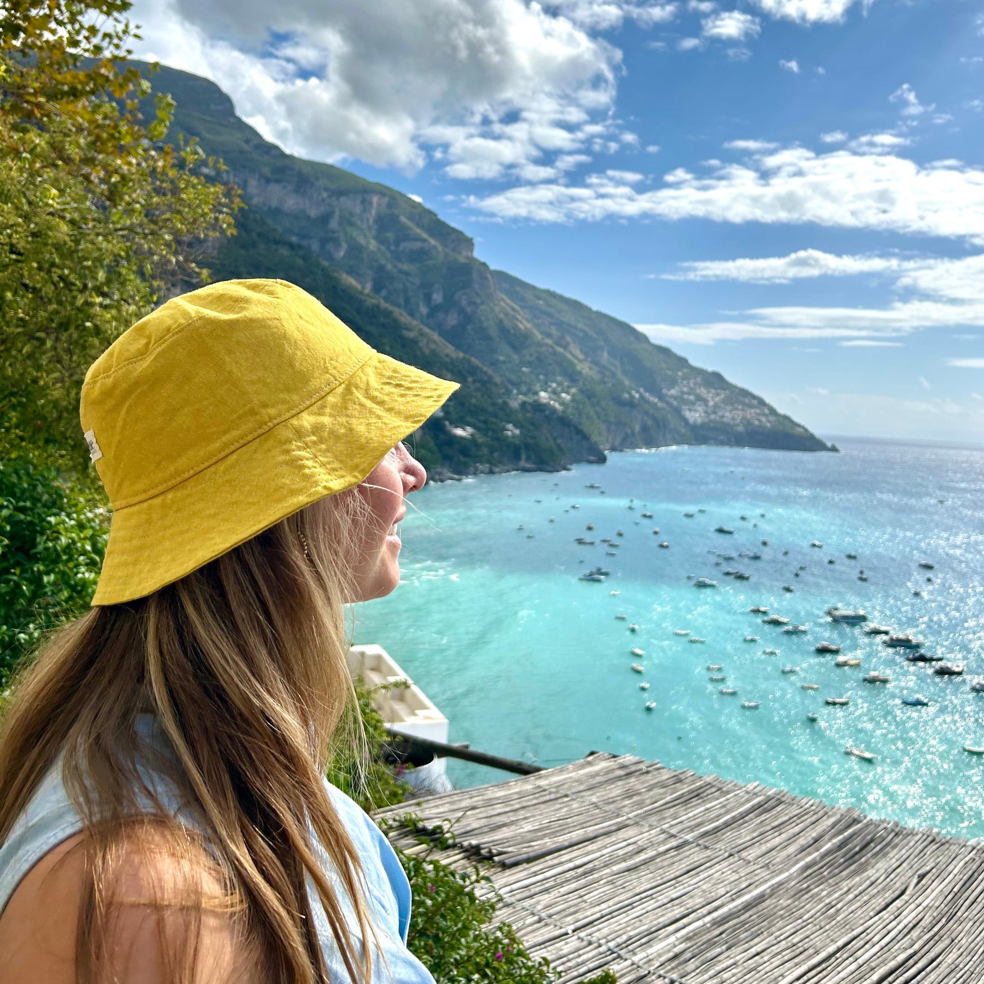 Person wearing a yellow hat overlooking a scenic lake with mountains and blue sky.