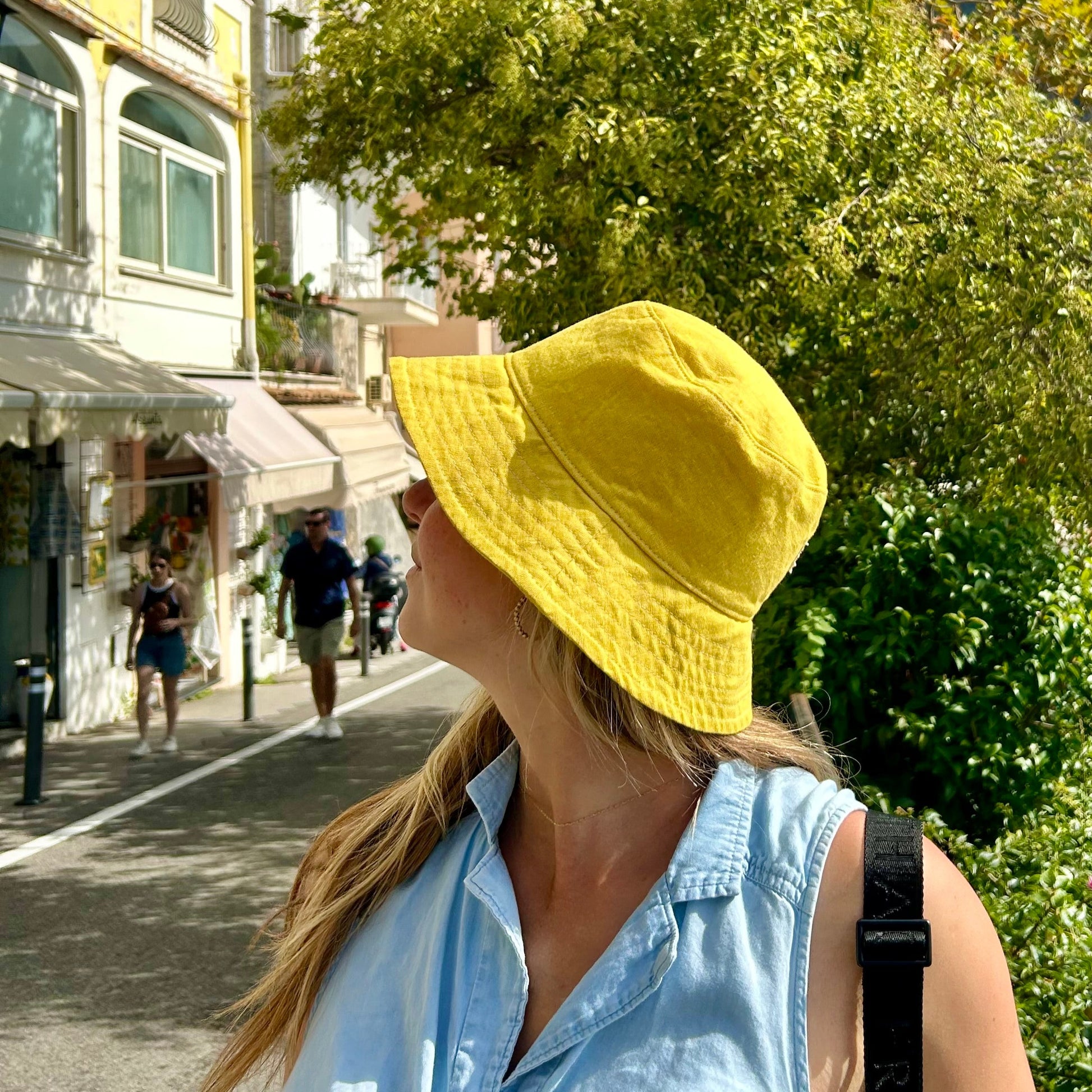 Woman wearing a yellow hat in an urban setting with trees and mountains in the background