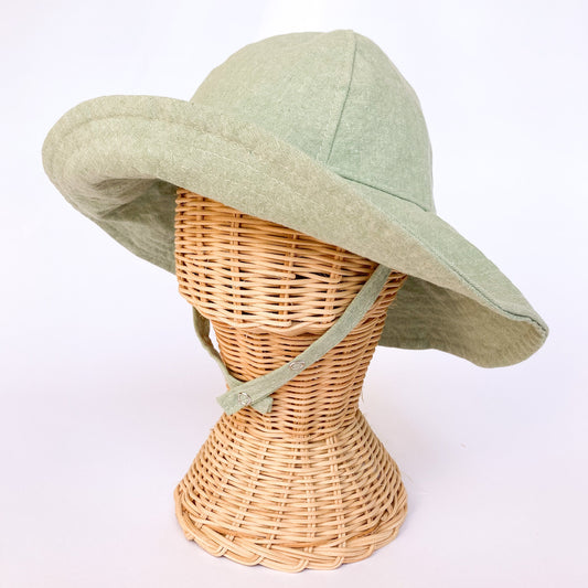 Wide brim light seafoam green colored linen/cotton hand made sun hat for baby on rattan head mannequin. Chin straps close with two snaps for adustable fit. Brim can flip up or stay down with ease.