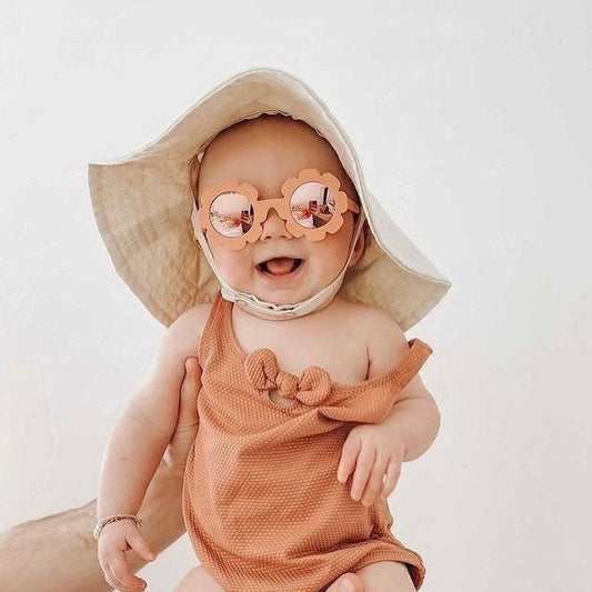 Wide brim natural beige colored linen/cotton hand made sun hat on baby. Chin straps close with two snaps for adustable fit. Brim can flip up or stay down with ease.