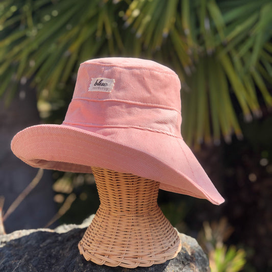 Blush Pink Corduroy Wide Brim Sun Hat on rattan mannequin head outside.