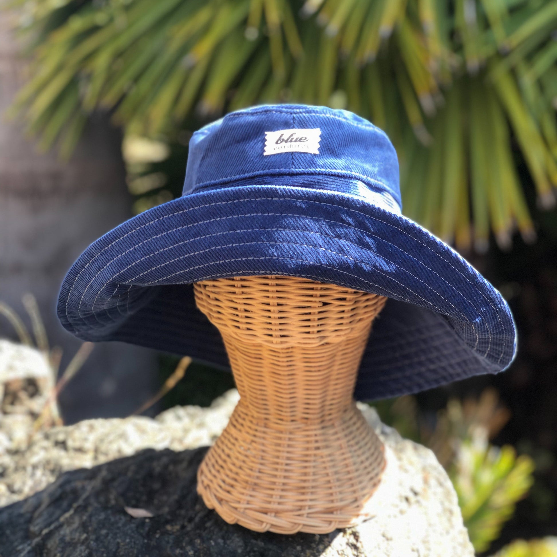 Bright Blue corduroy wide brim bucket hat outside on rattan mannequin head.
