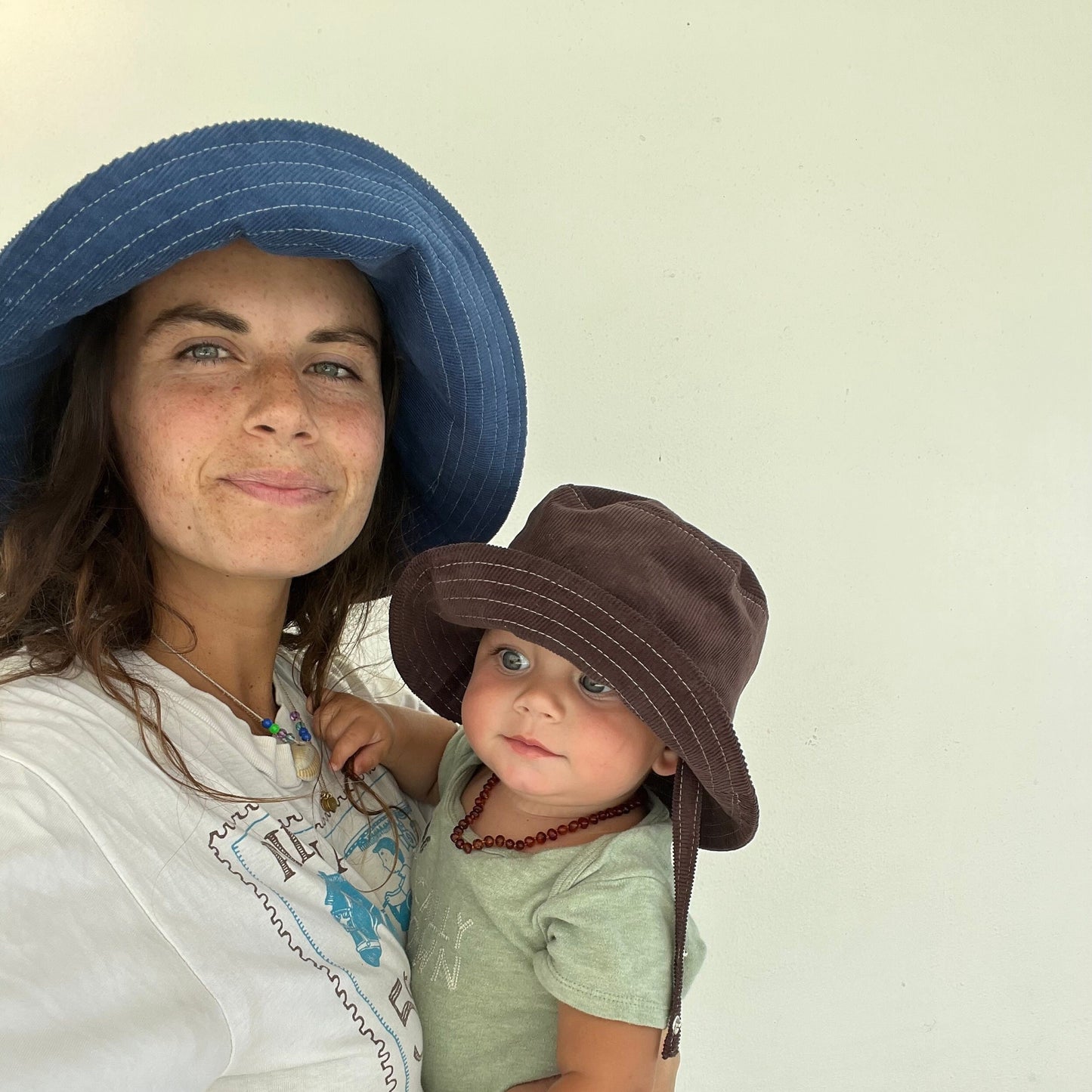 Mom wearing blue wide brim sun hat holding baby with brown sun hat