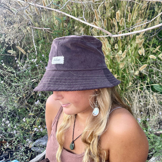 Brown corduroy bucket hat on blonde girl sitting outside.